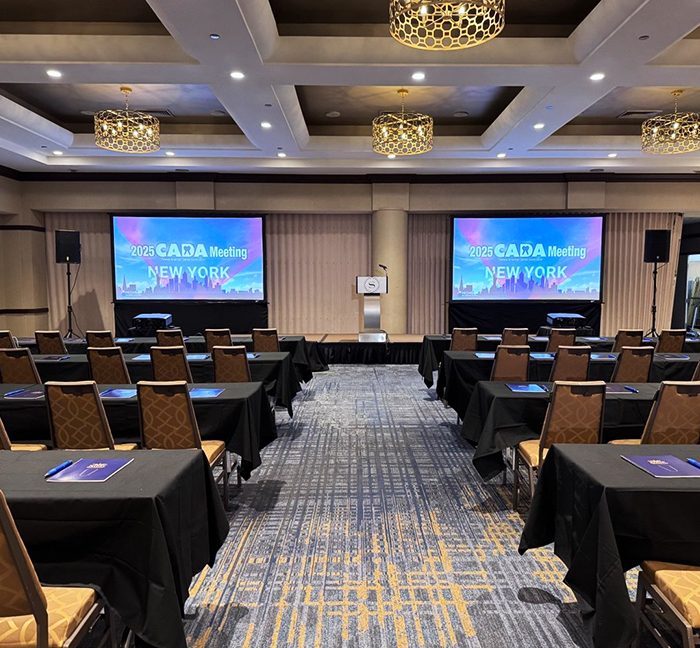 Conference room with dual projection screens prepared for the 2025 CADA meeting